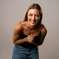 Thumbnail for Smiling woman with long brown hair wearing a black top and denim jeans, expressing joy and happiness.